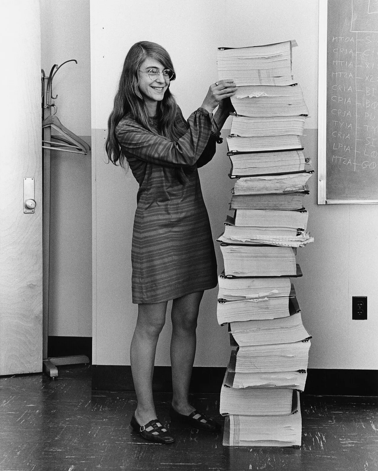 Margaret Hamilton en 1969, sonriente, junto a una pila de listados de código impresos casi tan alta como ella